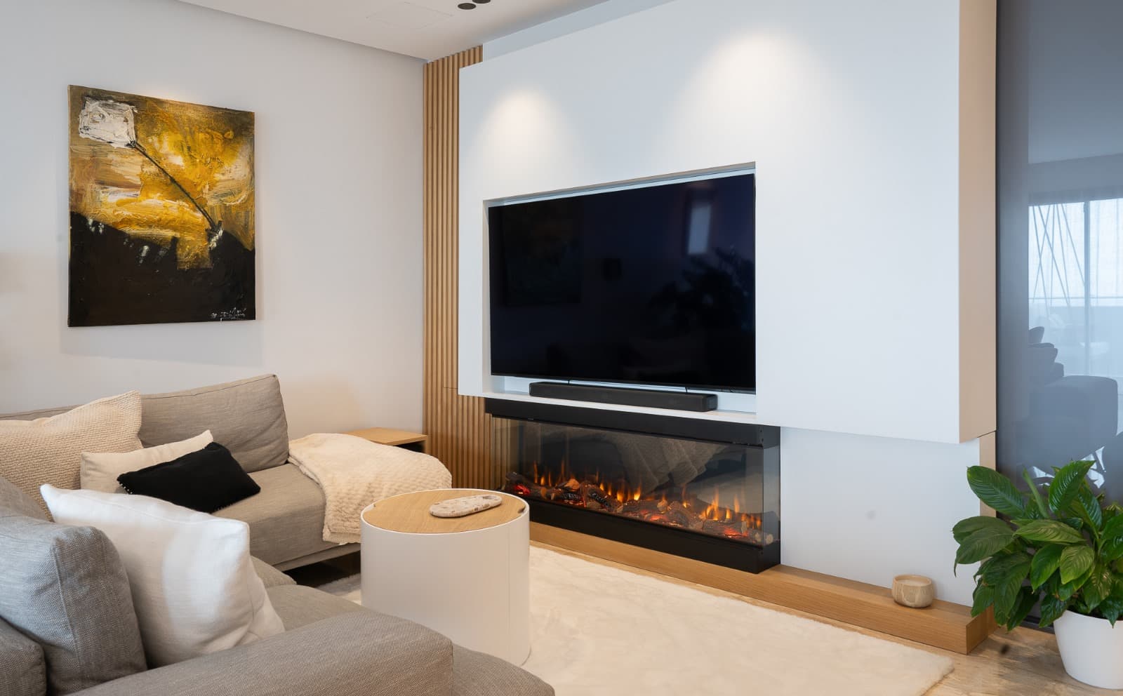 Lit panoramic electric fireplace below the TV, in a white living room with a grey sofa