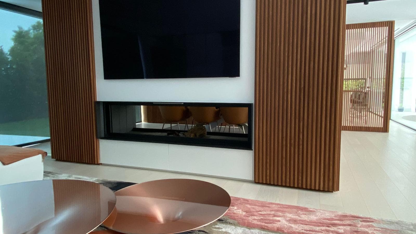 Chimenea de leña a medida de doble cara entre listones de madera, en un salón de Barcelona