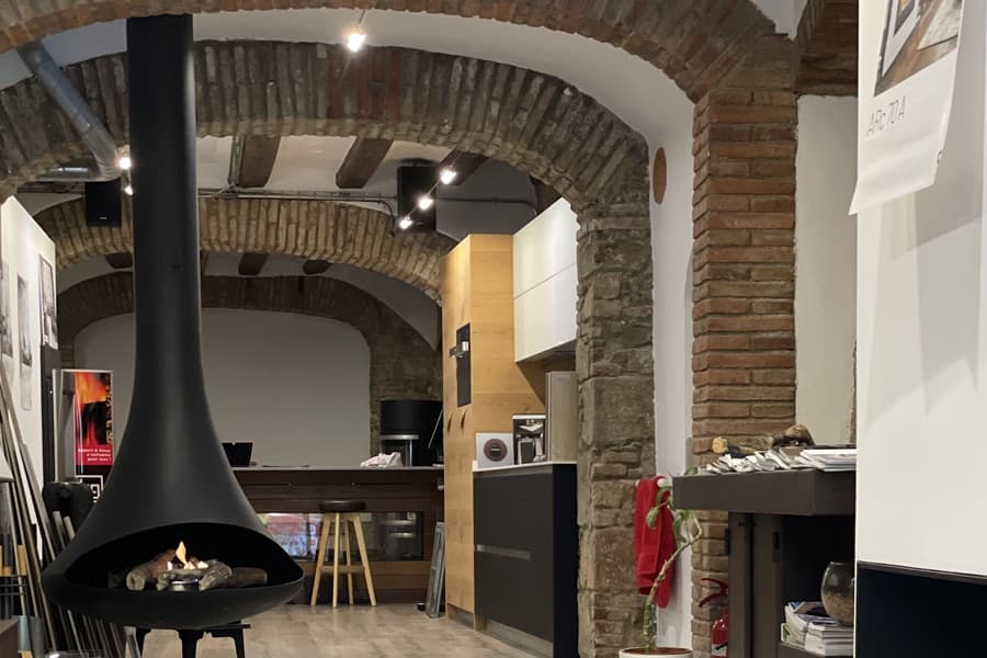 Black steel bioethanol fireplace suspended from the ceiling, in a space with exposed brick arches