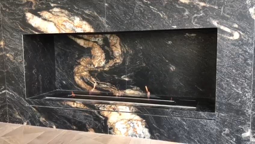 Built-in bioethanol fireplace: lit linear burner inside a recess in a wall clad in veined black