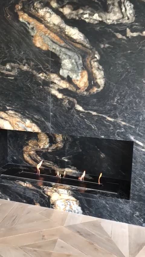 Close-up of a lit linear bioethanol burner in a wall clad in veined black