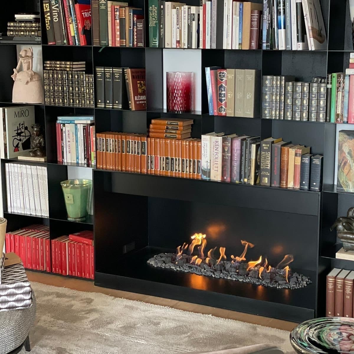 Salón de Barcelona con una chimenea de gas atmosférica encendida bajo una librería de hierro negro hecha a medida