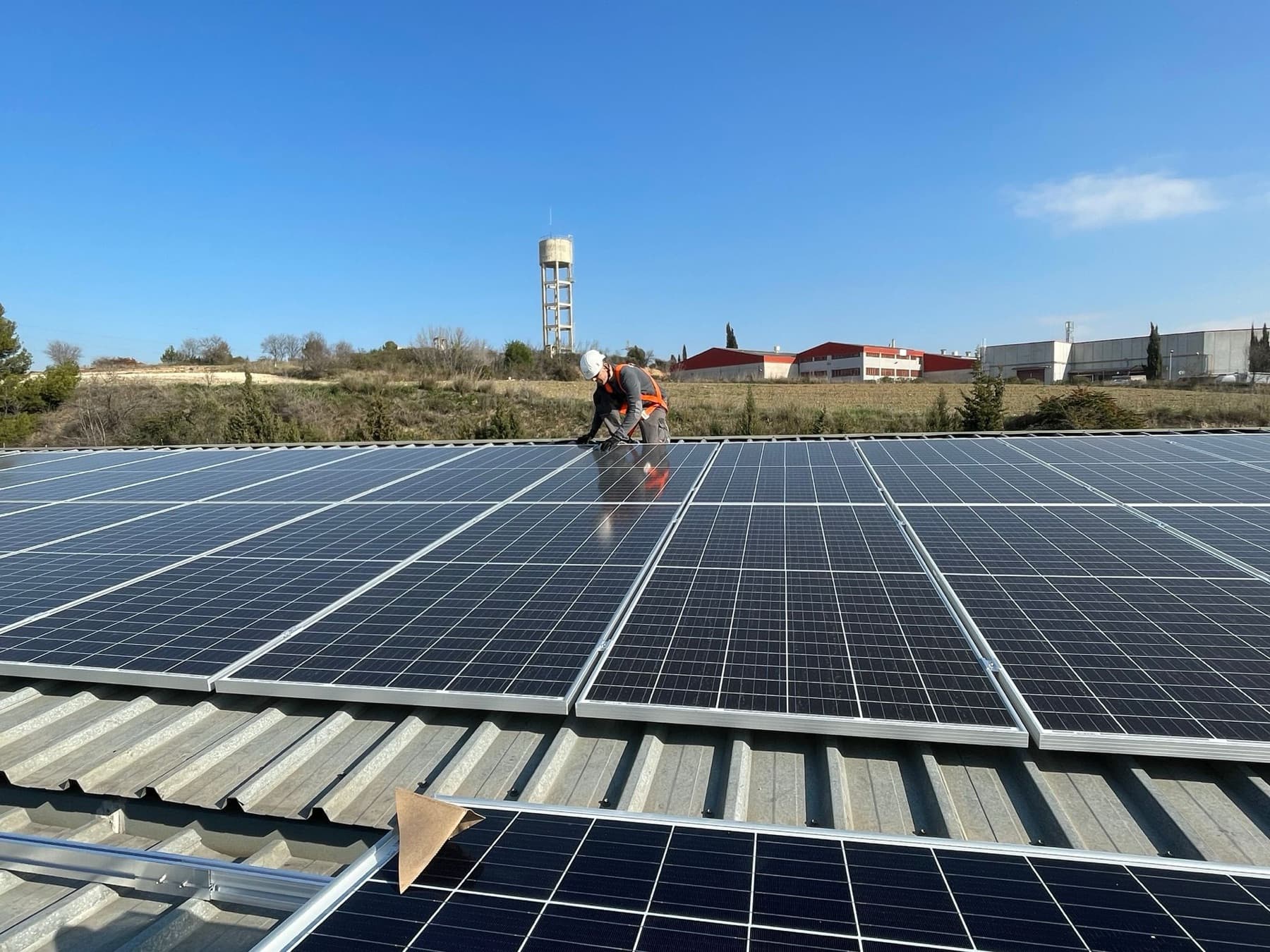 Photovoltaic solar panels on the metal roof of an industrial building, with a technician working among the panels