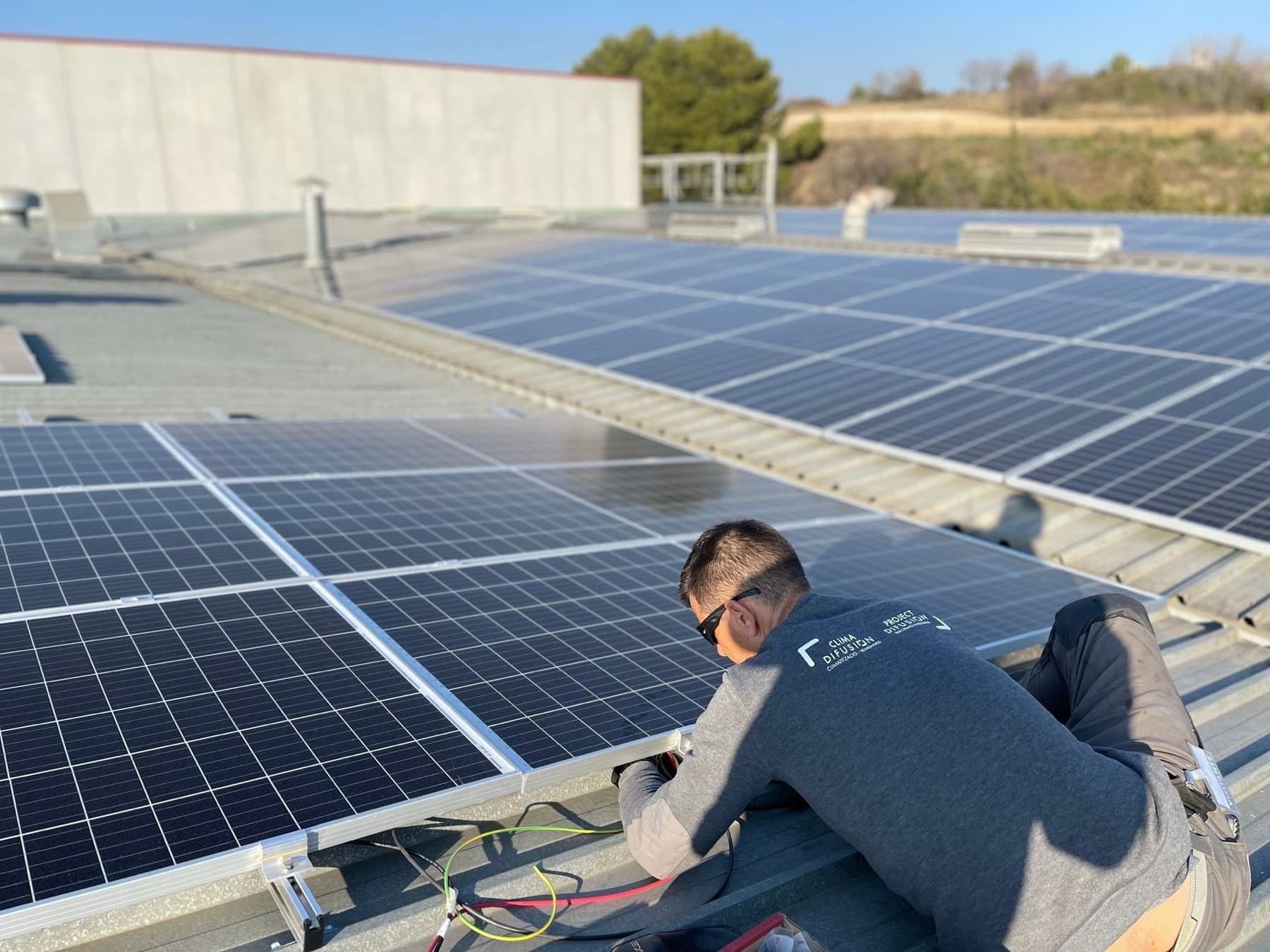 Technician in Clima Difusión and Project Difusión workwear connecting solar panels on the roof of an industrial building