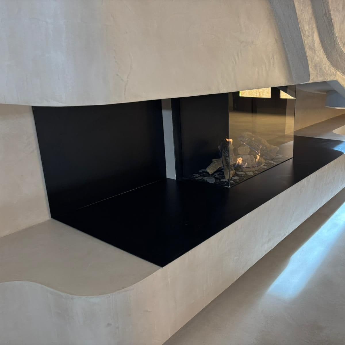 Chimenea a medida de gas integrada en una pared con relieve escultórico, con la caja negra y el banco corrido