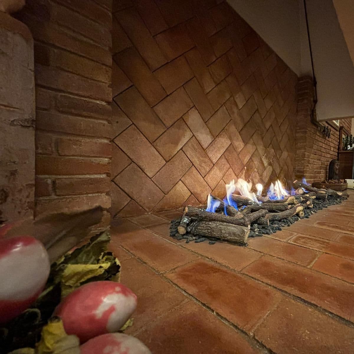 Instalación de chimenea de gas en un antiguo hogar de leña de ladrillo, con la llama encendida sobre los troncos cerámicos