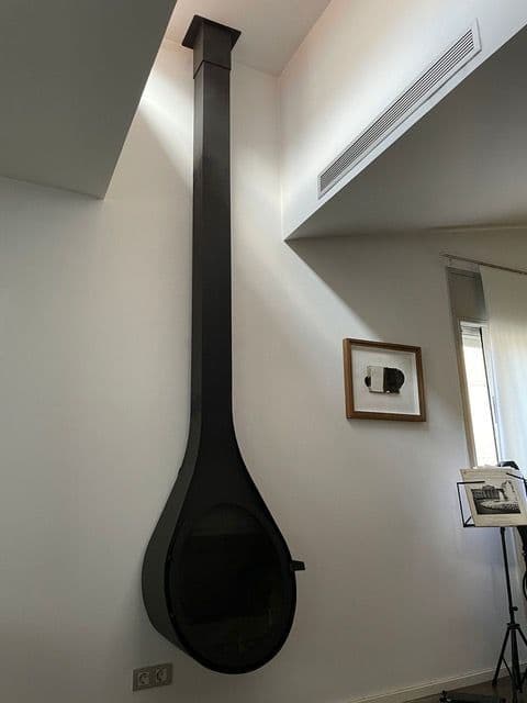Chimenea de leña colgada con forma de gota y tubo visto junto a una pared blanca