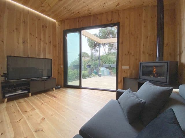 Estufa de leña tipo casete en la esquina de un salón revestido de madera, junto al ventanal