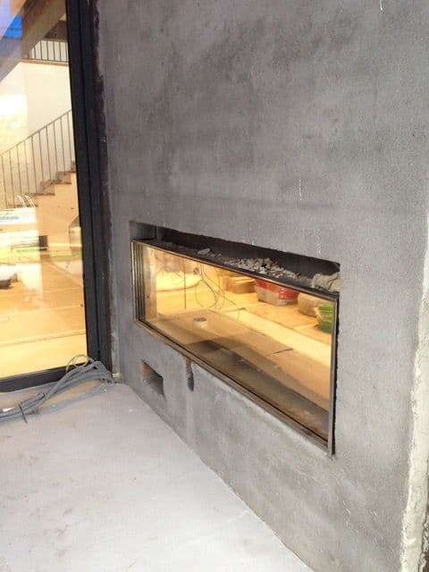 See-through gas fireplace during the building work, in a grey wall that is not yet finished