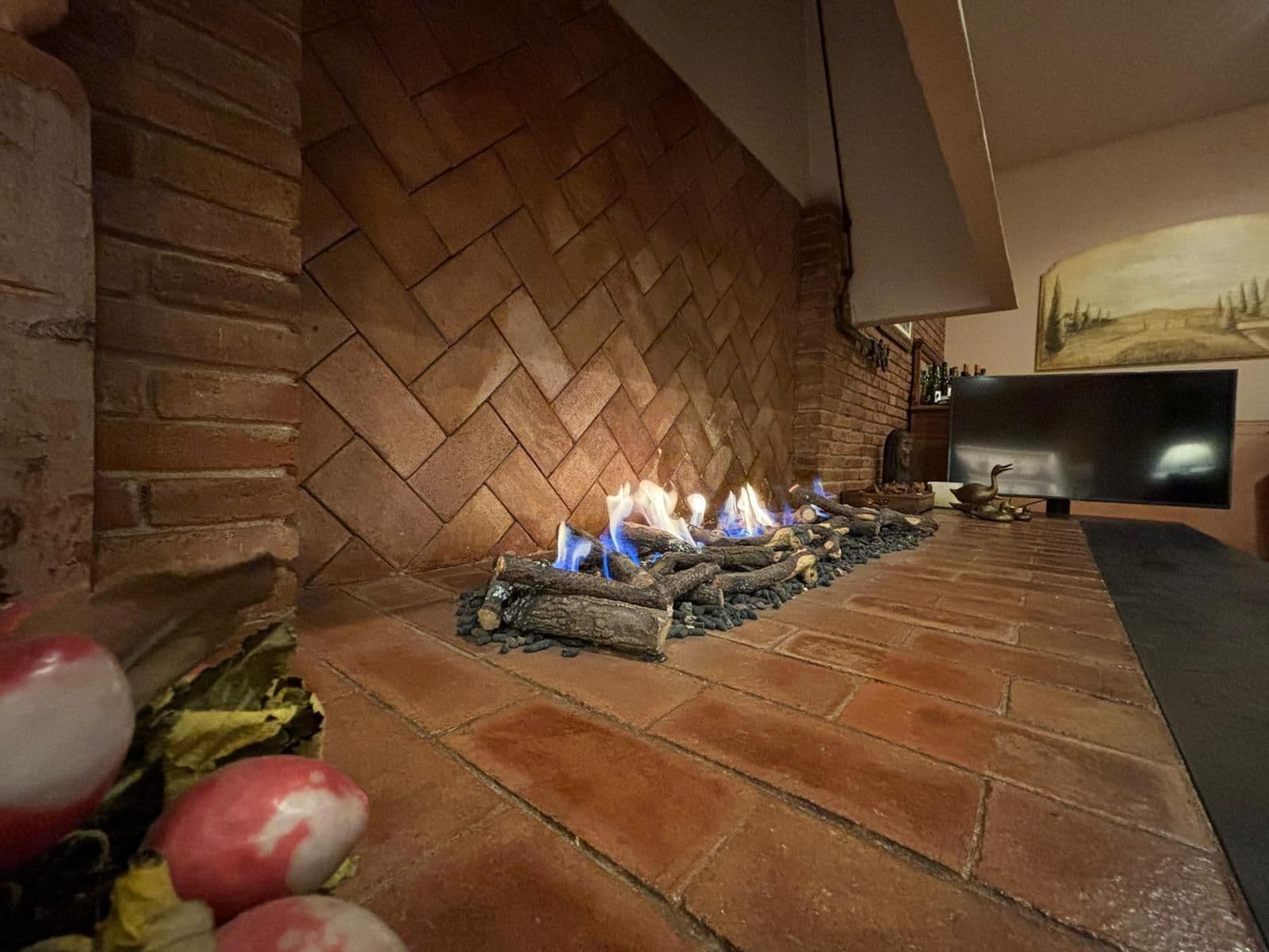 Antigua chimenea de leña de ladrillo transformada en chimenea de gas atmosférica, con troncos cerámicos encendidos