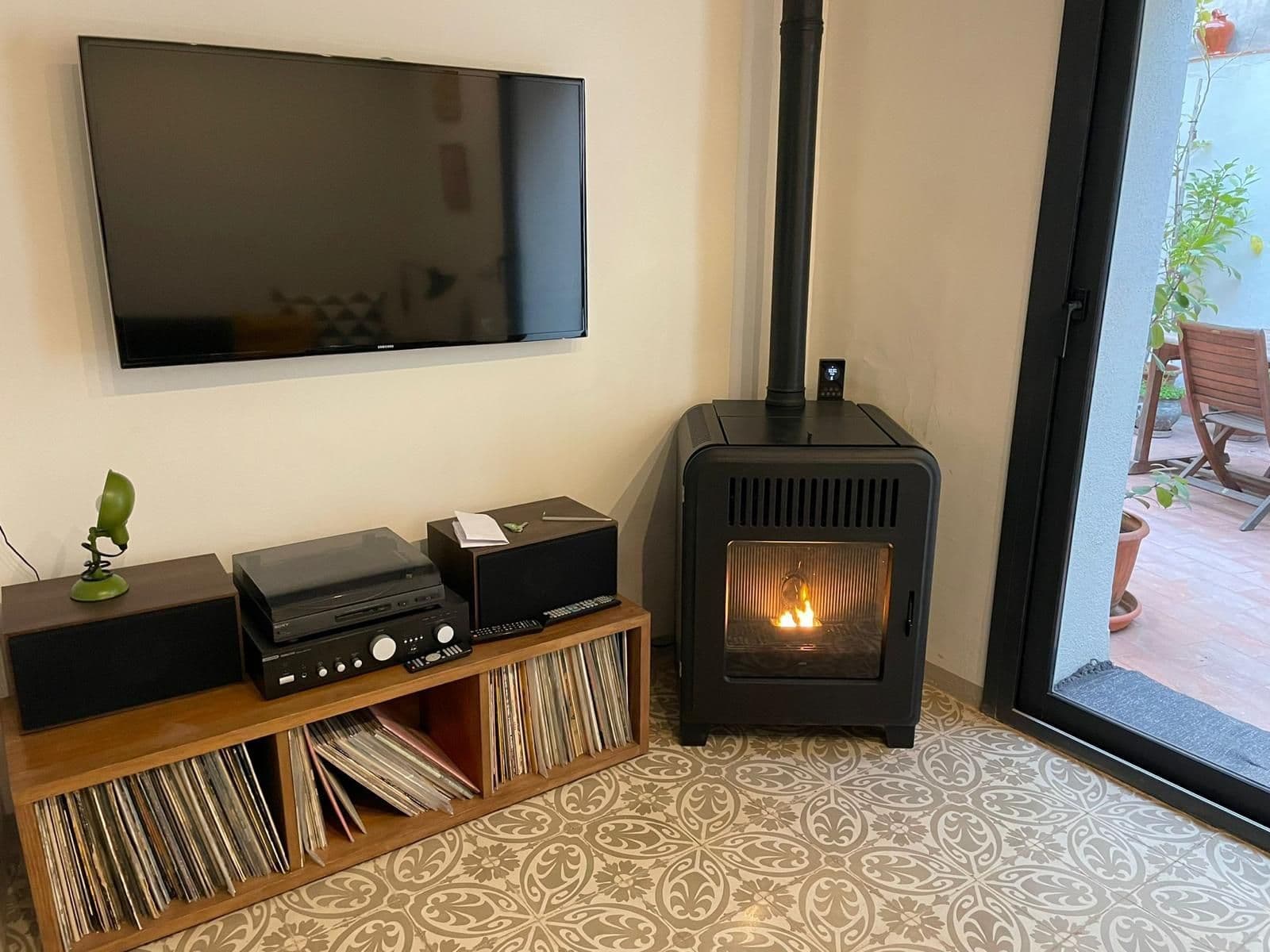 Estufa de pellet compacta encendida junto al televisor y a un mueble de vinilos, en un salón con suelo hidráulico