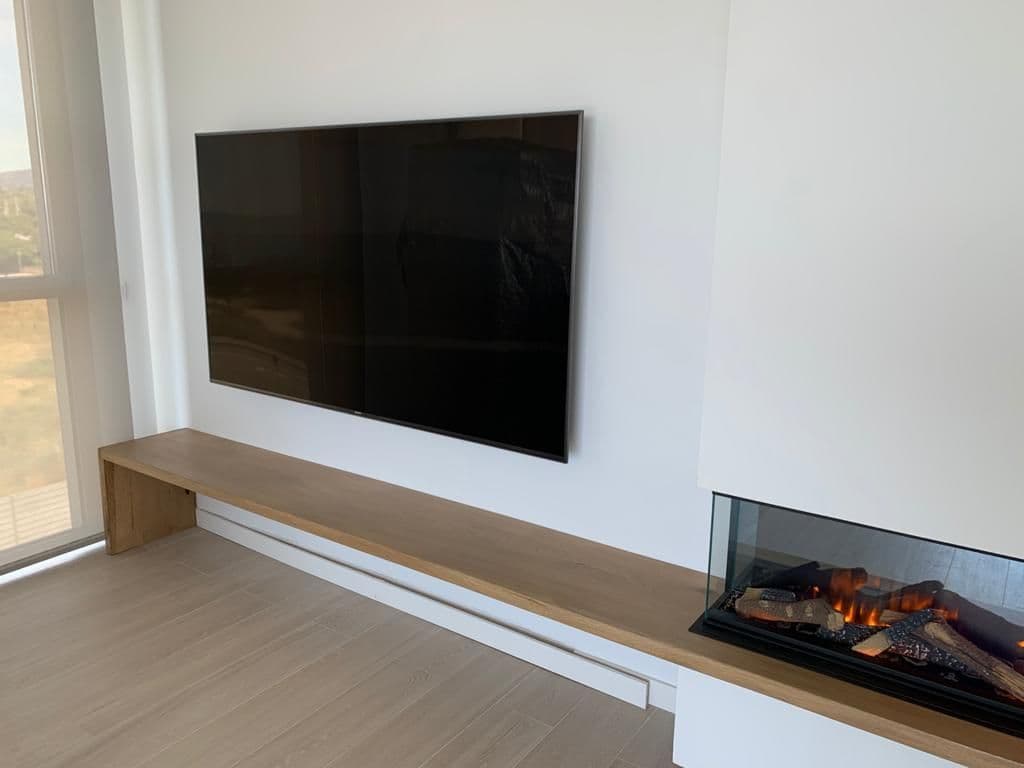 Chimenea eléctrica integrada en una bancada de madera hecha a medida bajo el televisor