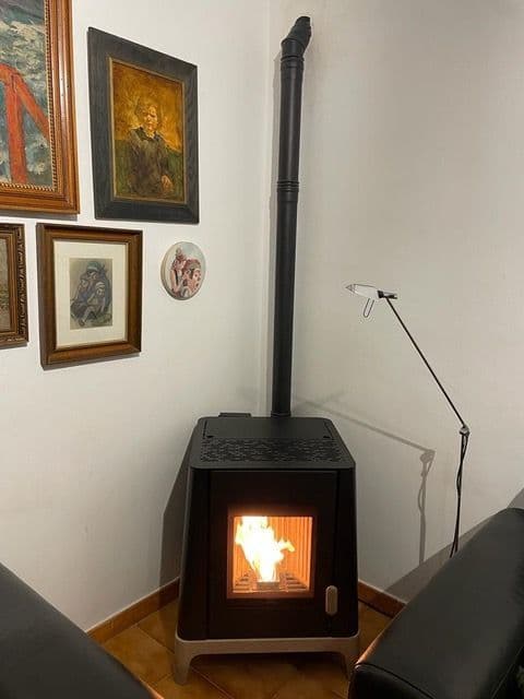 Estufa de pellet en la esquina de un salón con cuadros, con el tubo de salida de humos vertical