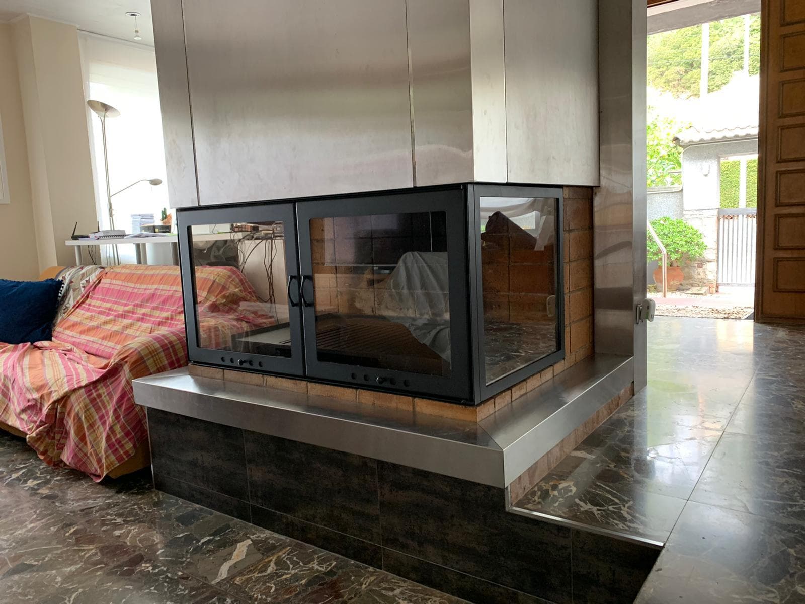 Chimenea de leña con cerramiento acristalado sobre una bancada, instalada en el centro de un salón
