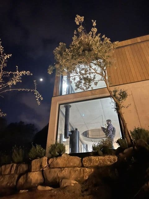 Estufa de leña giratoria encendida, vista por la noche desde el jardín a través del ventanal
