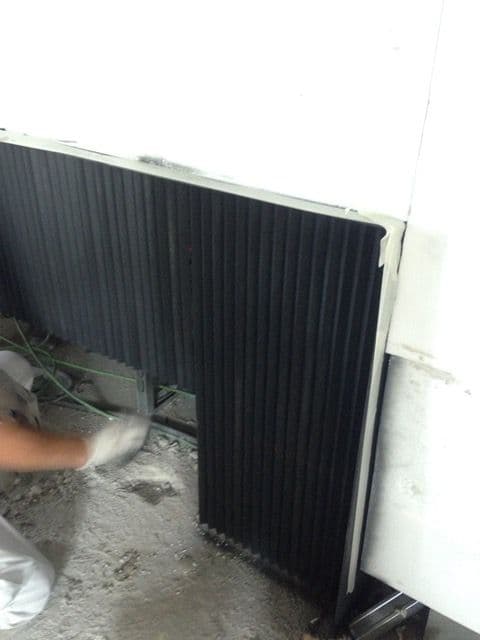 Installer fixing a black iron angle back at the foot of a white wall, on site for a bioethanol fireplace
